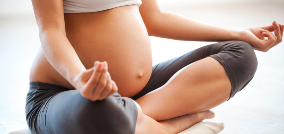 Meditating on maternity. Close-up of pregnant woman meditating while sitting in lotus position