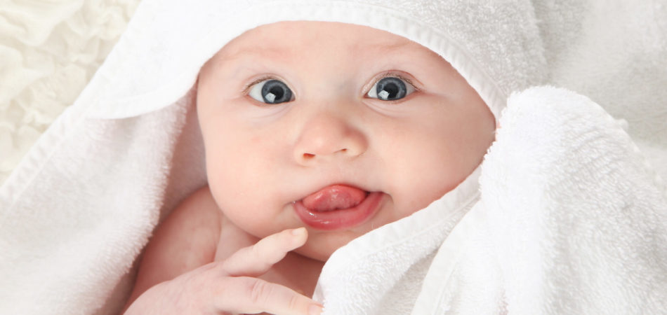 Close up portrait of a cute baby wrapped in a white towel with tongue sticking out