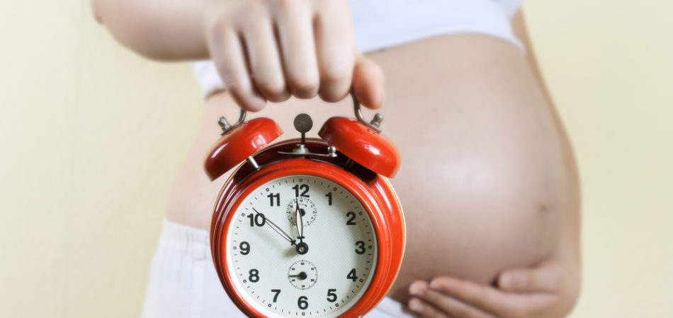 Pregnant woman holding alarm clock.