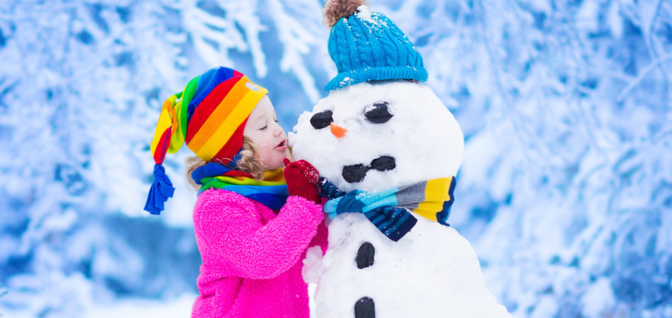 Funny little toddler girl in a red knitted Nordic hat and warm coat playing with a snow. Kids play outdoors in winter. Children having fun at Christmas time. Child building snowman at Xmas.