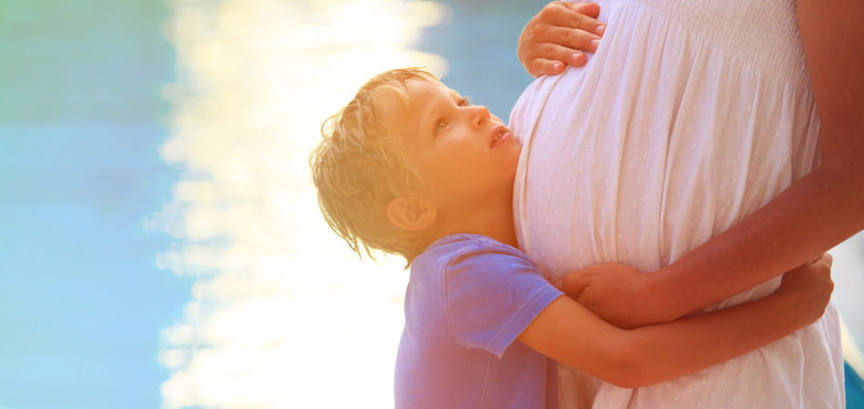 little boy hugging pregnant mother tummy at beach, happy family