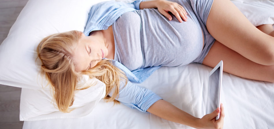 Pregnant woman lying in bed and watching movies on tablet computer