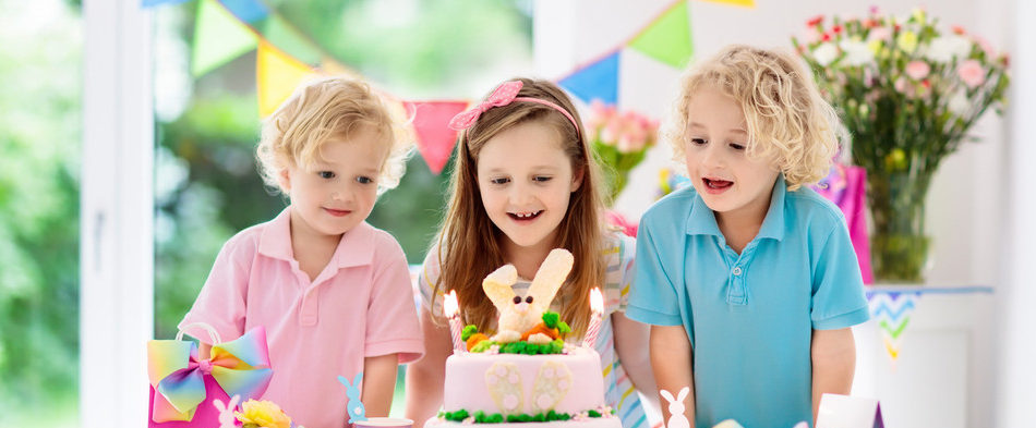 Kids birthday party. Children blow out candles on pink bunny cake. Pastel rainbow decoration and table setting for kids event, banner and flag. Girl and boy with birthday presents. Family celebration.