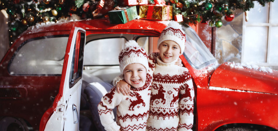 Two boys in xmas sweaters near a red retro car. Christmas, New Year concept.