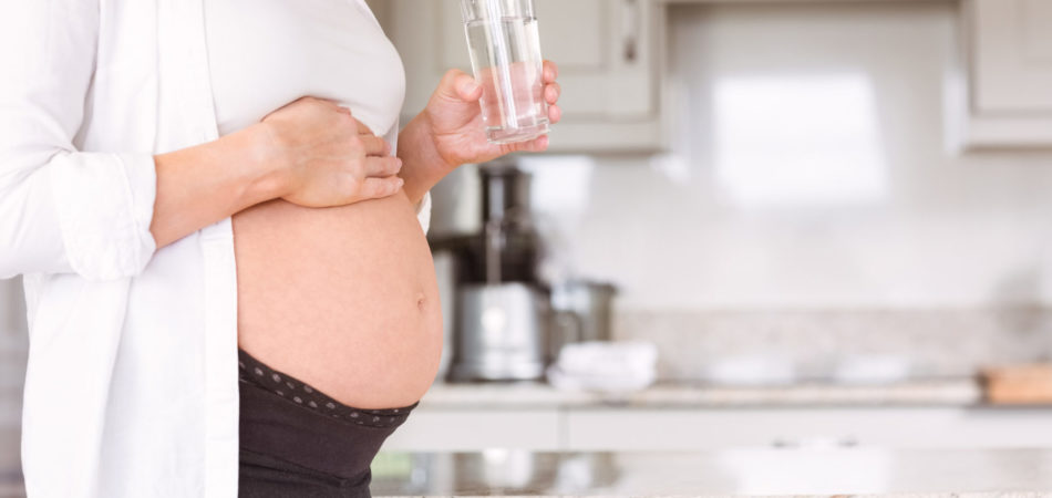 Pregnant woman drinking glass of water at home in the kitchen