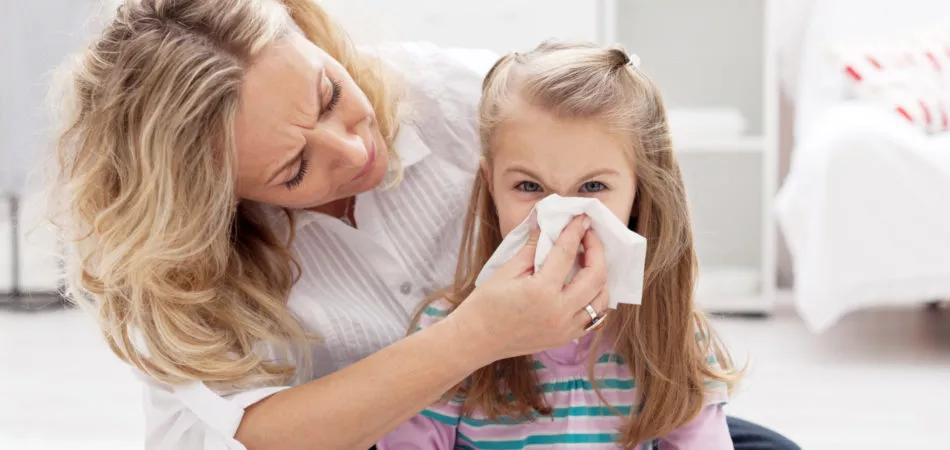 Woman at home blowing the nose of her little girl