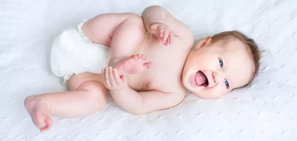 Funny laughing baby wearing a diaper playing with her feet