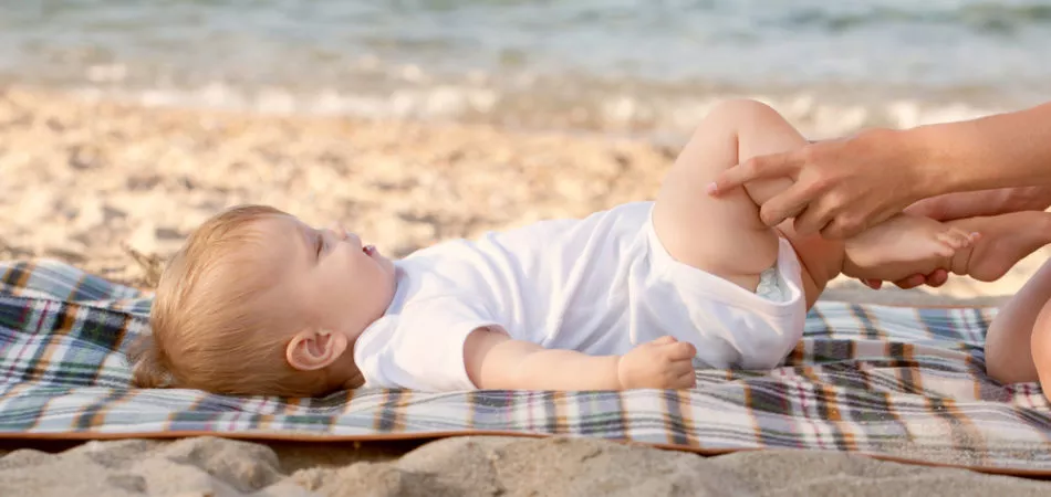 Baby massage on the beach. Mother playing with kid legs, baby smiling.
