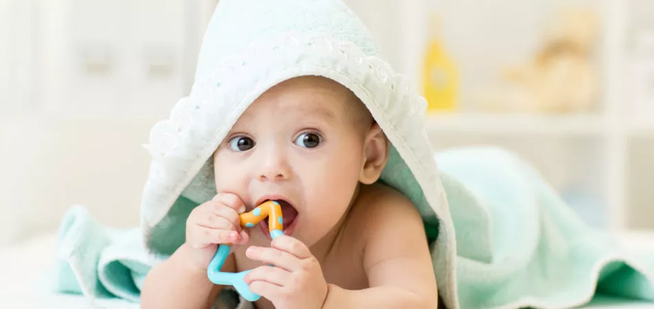 baby with teether in mouth under bathing towel at nursery
