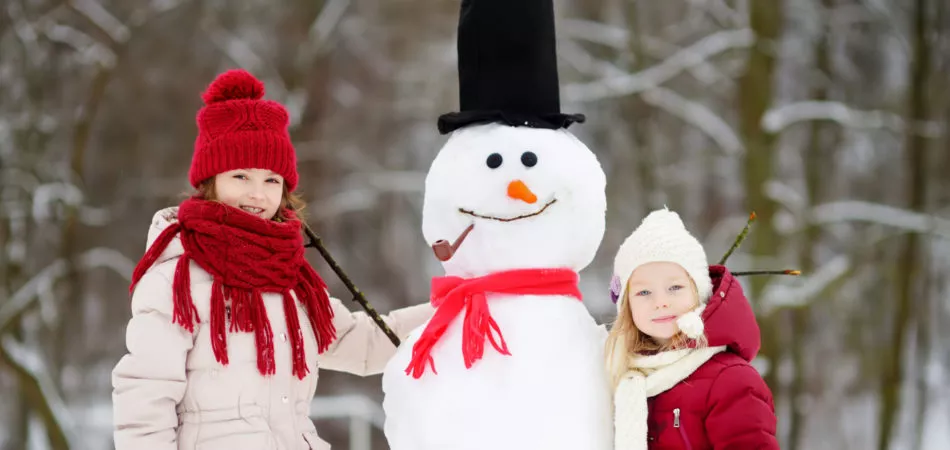 Two adorable little girls building a snowman together in beautiful winter park. Cute sisters playing in a snow. Winter activities for kids.