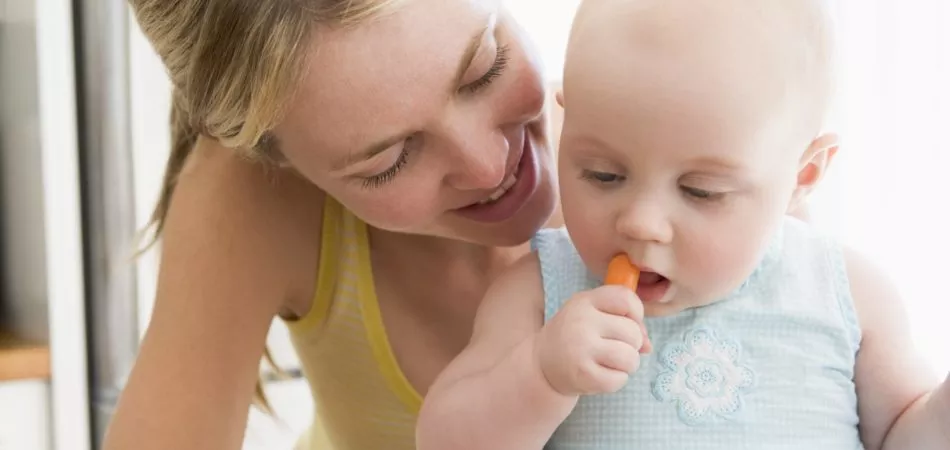 Mother and baby in kitchen eating carrot